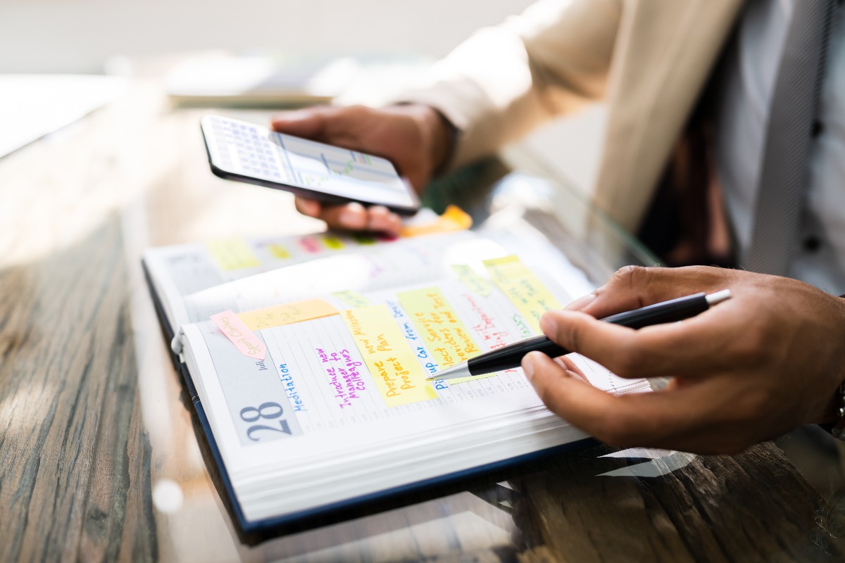 Personne essayant d'organiser un événement IT avec son téléphone et un agenda