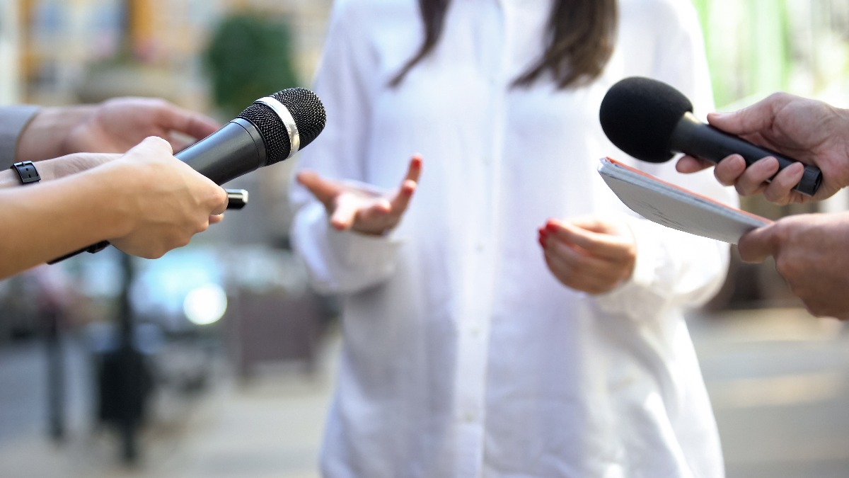 Personnes tendant des micros vers une dame répondant à des questions