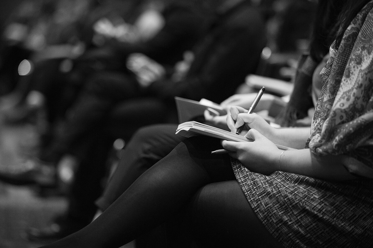 Personne assise prenant des notes dans un cahier lors d'un événement IT